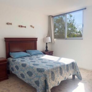 Habitación con cama matrimonial, cabecera de madera oscura, lámparas de noche y ventana grande con vista al exterior.