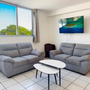 Sala con dos sofás grises frente a una ventana amplia con vista a árboles y una mesa de centro minimalista.