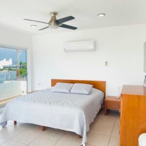 Zona de descanso en un loft moderno con cama matrimonial, muebles de madera cálida, aire acondicionado y salida directa a la terraza.