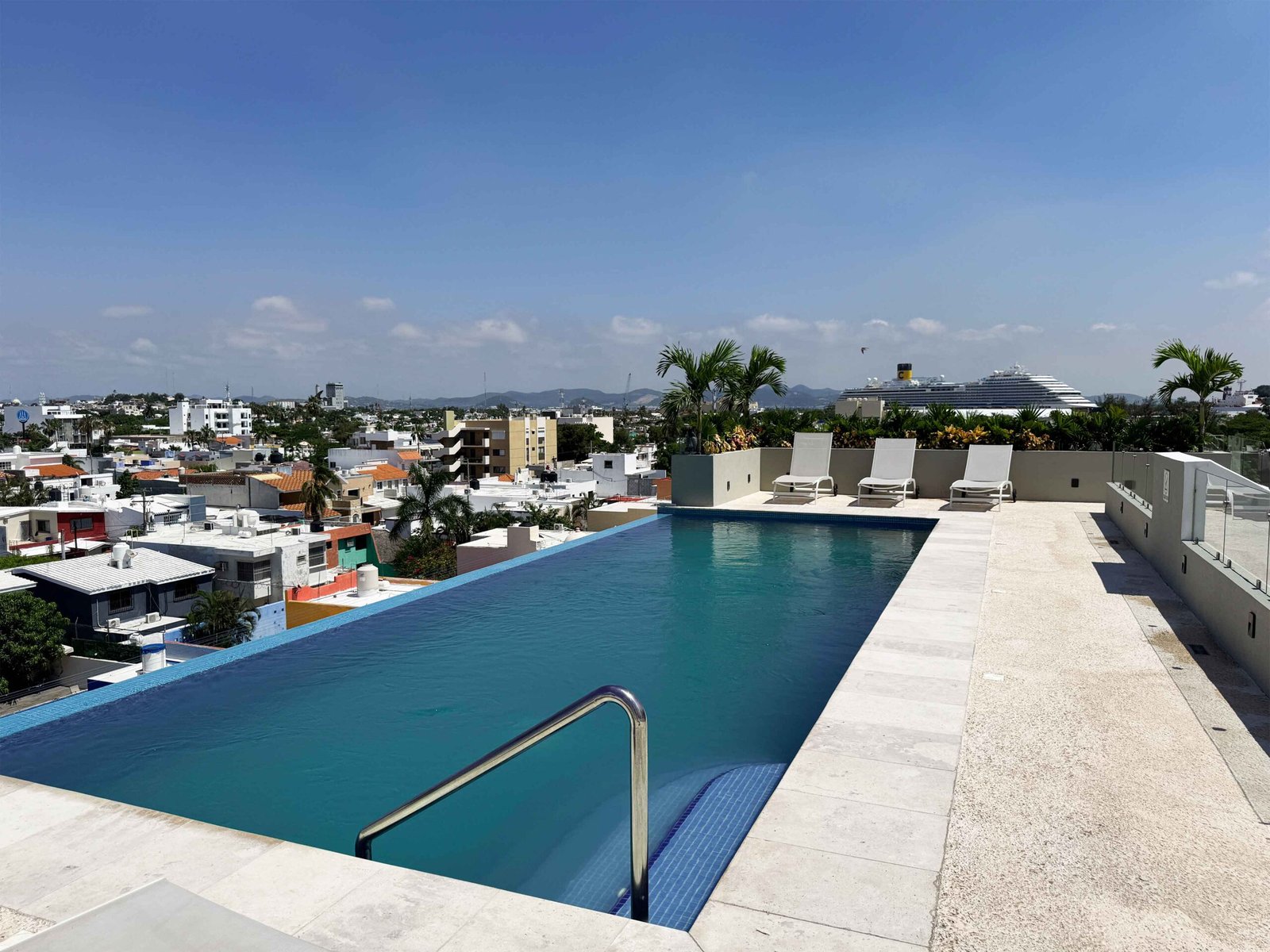 Alberca tipo infinity en el rooftop de Antara con camastros y vista al crucero en el horizonte.