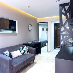 Sala de estar con sofá gris, cojines geométricos, mesa de comedor integrada para dos personas y vista al pasillo.