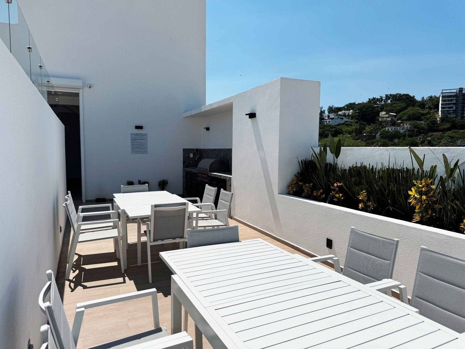 Comedor exterior moderno con mesas blancas y vegetación decorativa en el área común.