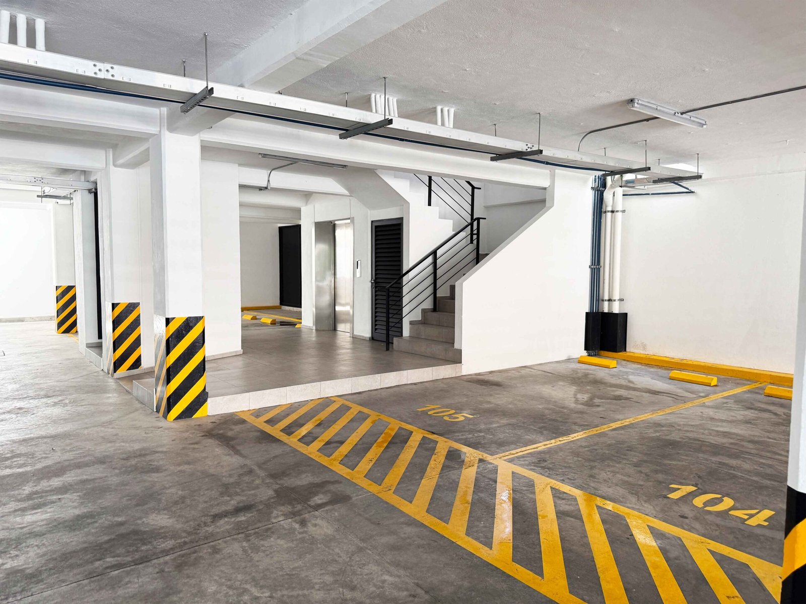 Área de estacionamiento techado con señalización y acceso a elevador.