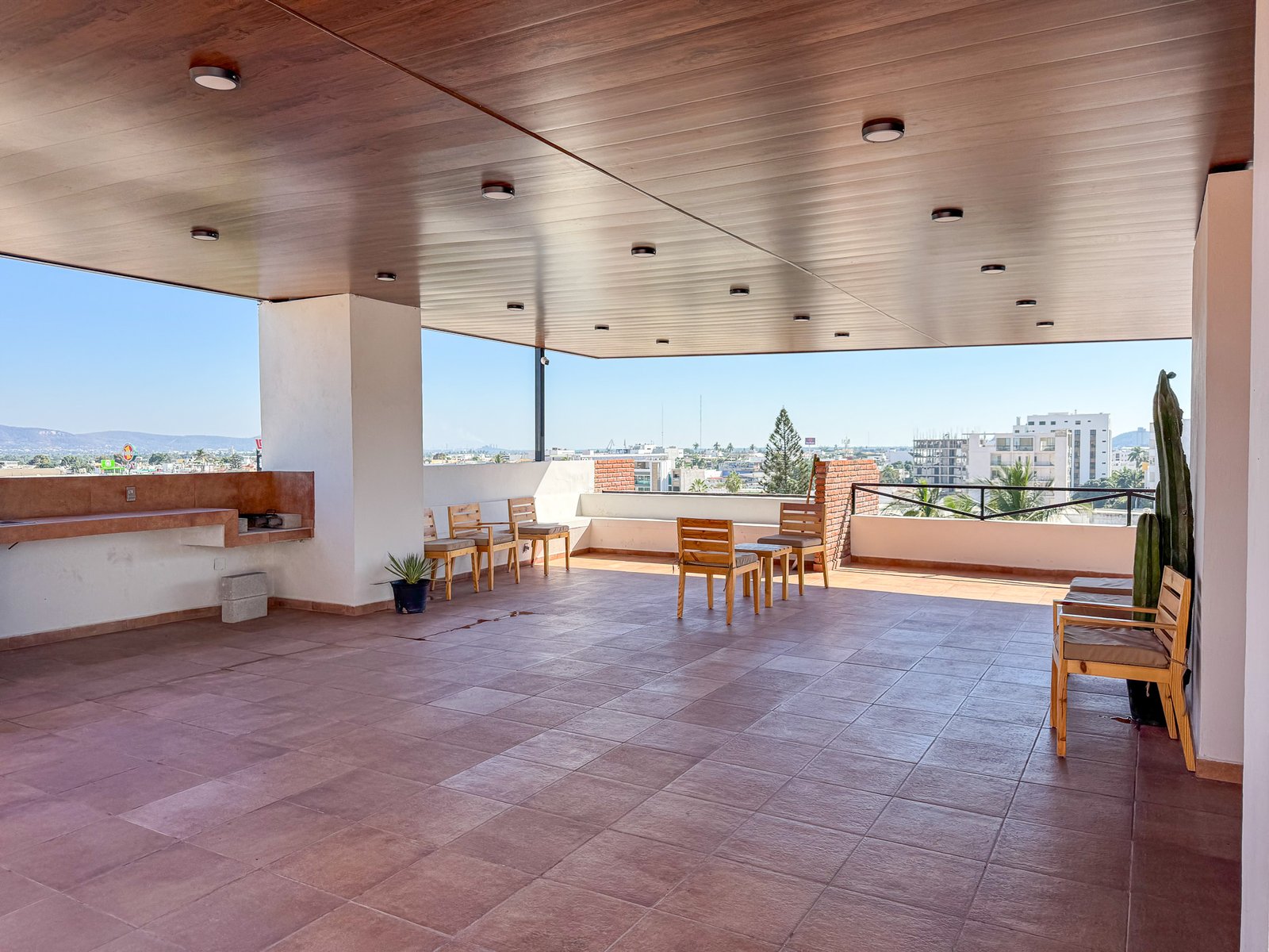 Terraza común techada con mobiliario de madera y área de asador en el desarrollo San Lorenzo.