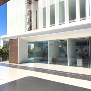 Vista frontal desde el pasillo exterior del local F2 en Laguna Plaza, destacando ventanales de piso a techo y fachada blanca.