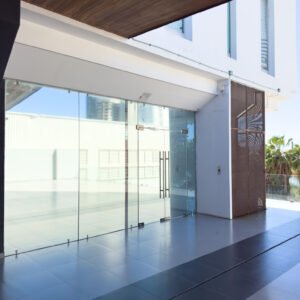 Fachada moderna de local comercial con ventanales de piso a techo y acceso principal en cristal templado.