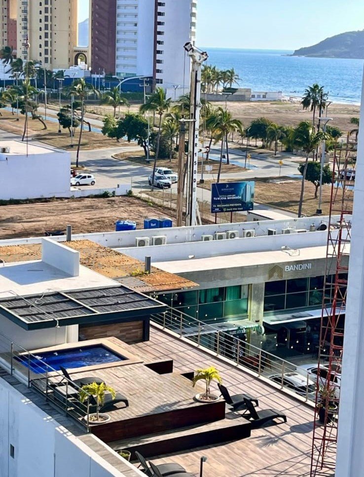Área de roof top en el edificio Manzara con jacuzzi, terraza de madera, camastros y vista a la ciudad y al mar.