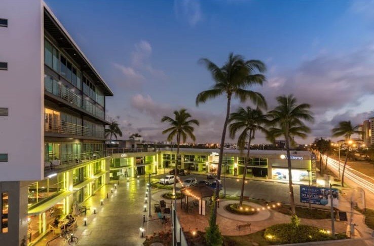 Vista nocturna de la plaza comercial y áreas comunes de Manzara iluminadas bajo un cielo de atardecer.