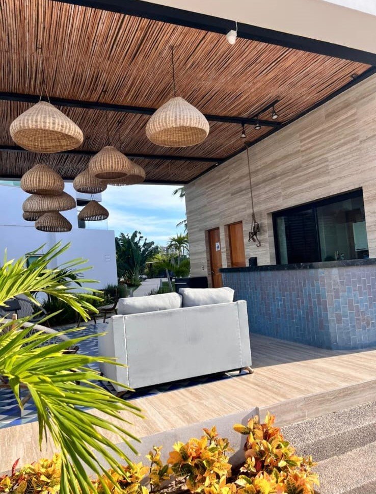 Área de bar exterior con techo de madera, lámparas de mimbre artesanales y barra de diseño moderno.