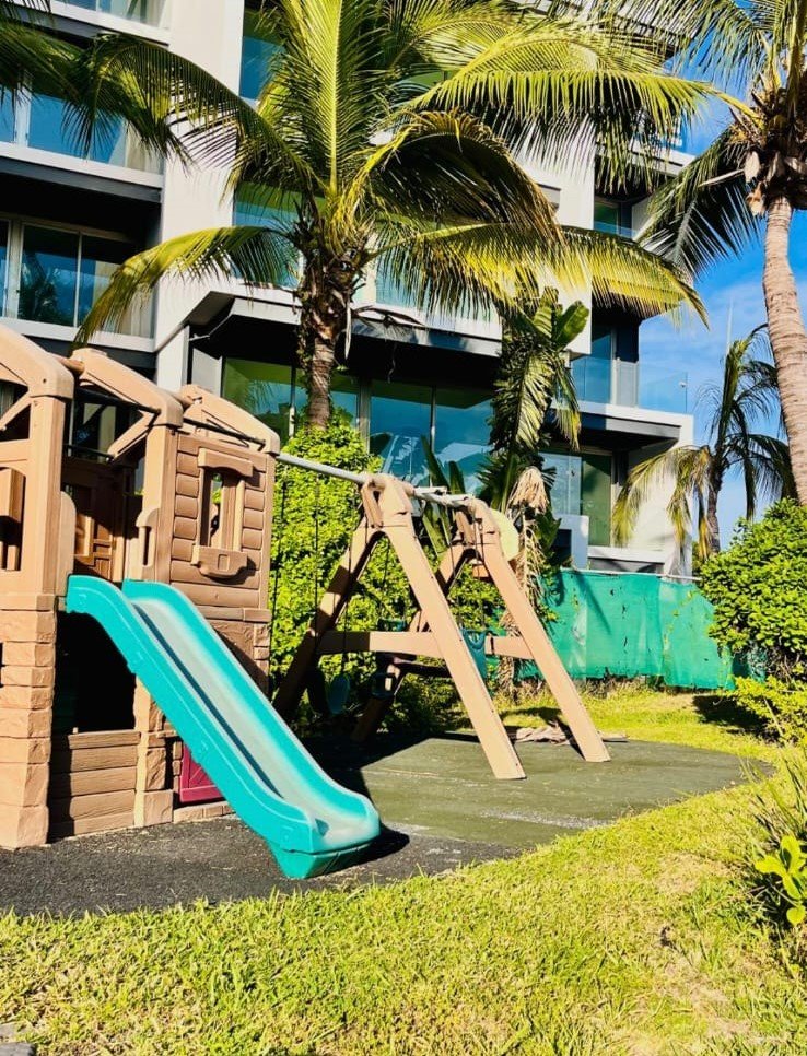 Parque infantil con resbaladilla y columpios rodeado de áreas verdes en Manzara.