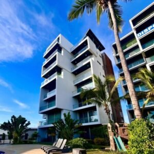 Fachada moderna de los departamentos Manzara Loft con balcones amplios, palmeras y cielo despejado.