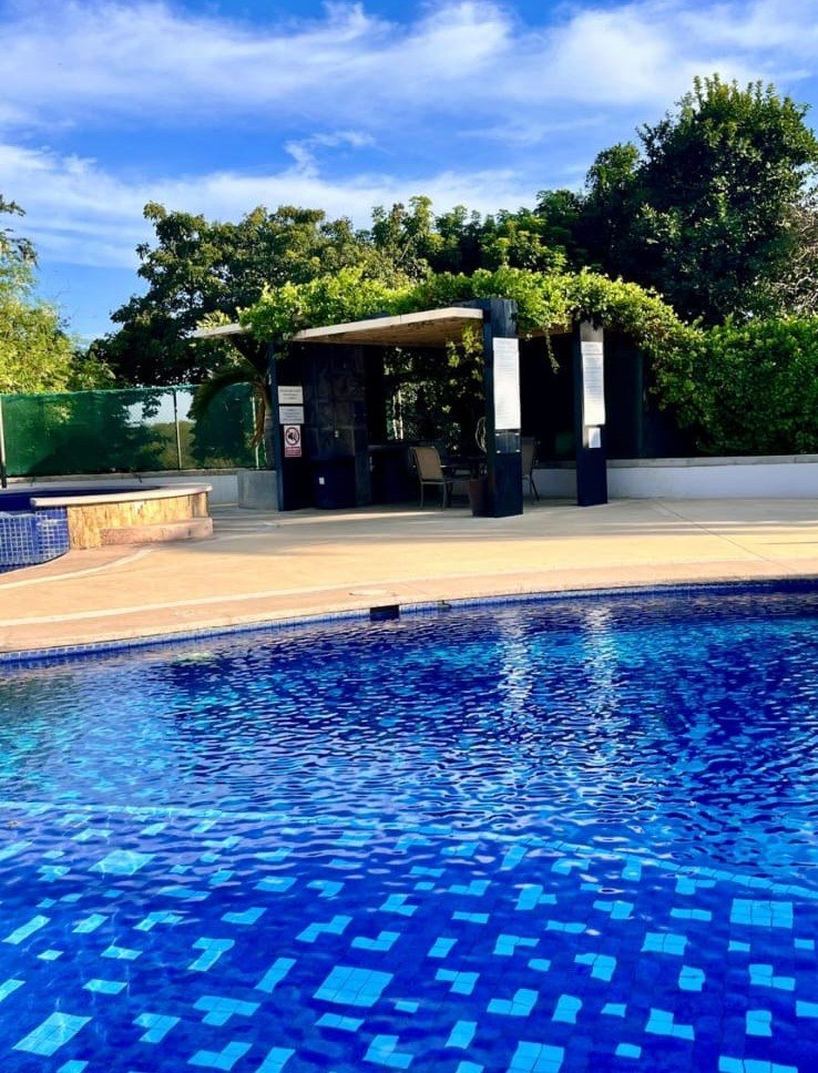 Área de sombra con pérgola de madera y vegetación junto a la alberca de Manzara.
