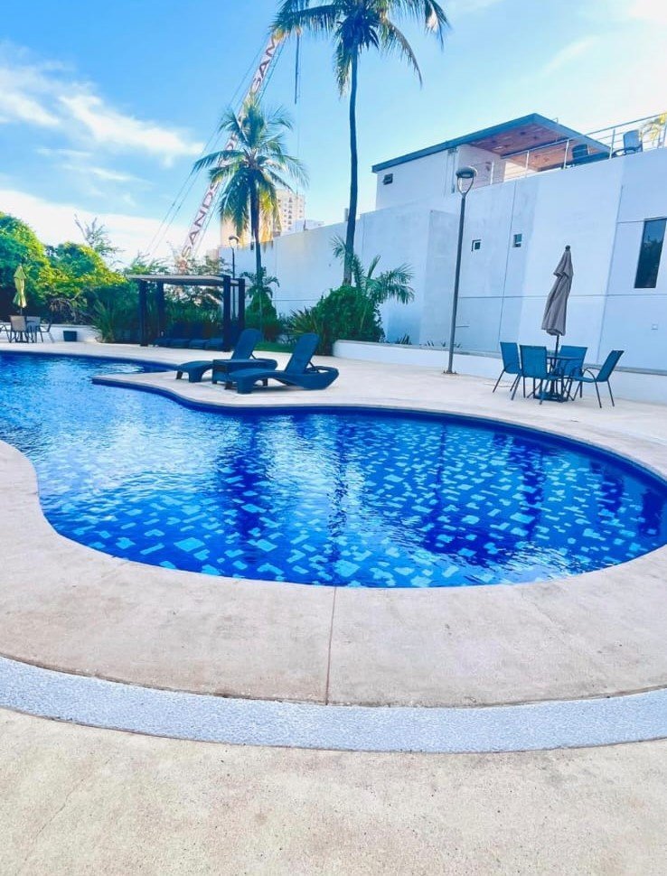 Camastros modernos y mesas con sombrilla en el área de solárium de la alberca en Manzara.