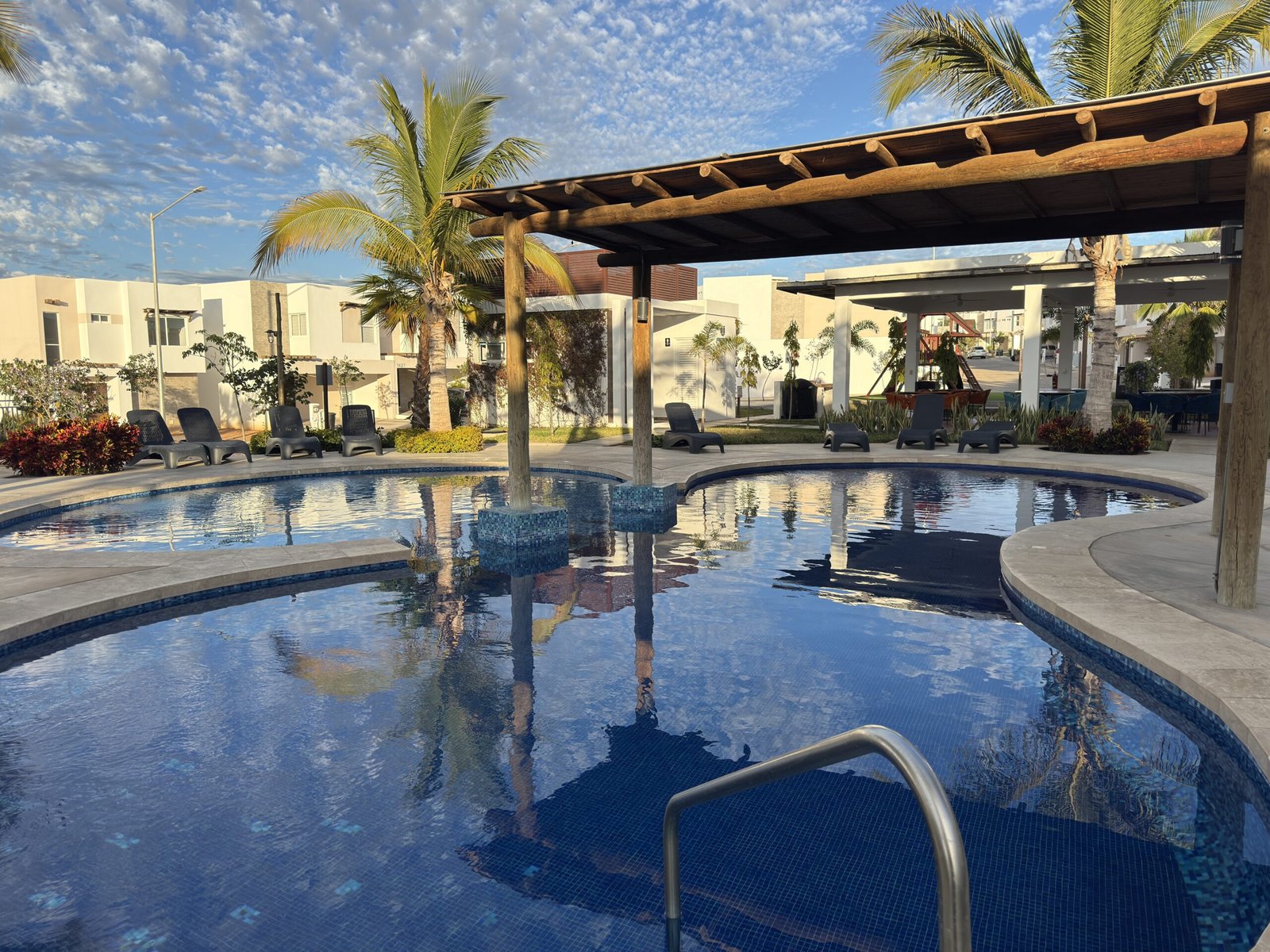 Zona de recreación exterior con palapas de madera, diseño de paisaje y alberca en el fraccionamiento Almarena 1314.